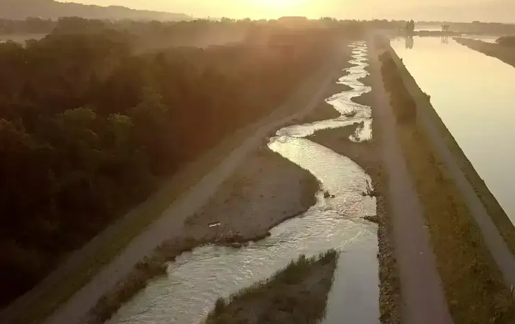 Sonnenuntergang über einem gewundenen Fluss, der durch eine grüne Landschaft fließt, mit weichem Sonnenlicht, das das Wasser erleuchtet.